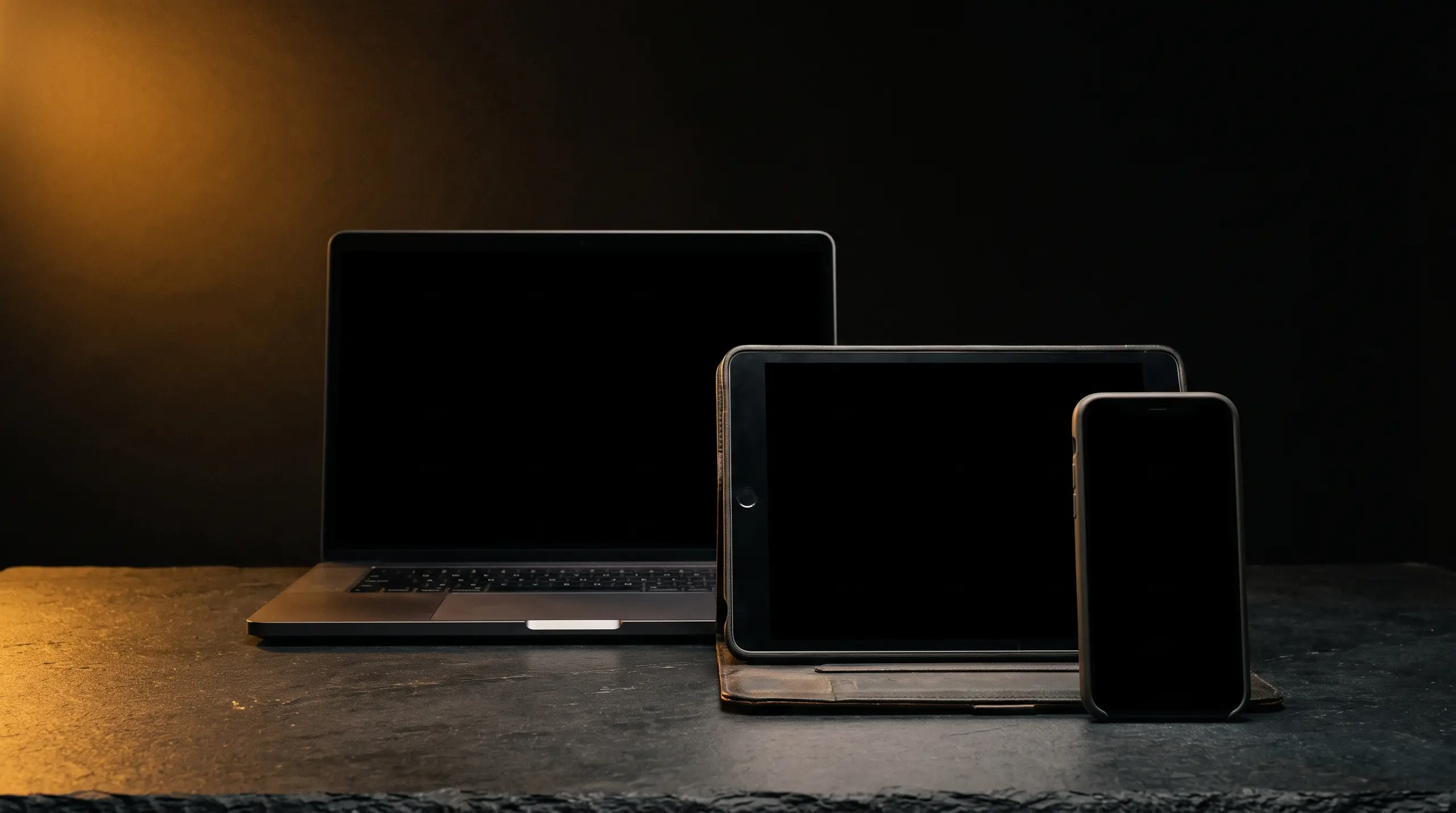 A laptop, tablet and phone arranged together, all screens blank